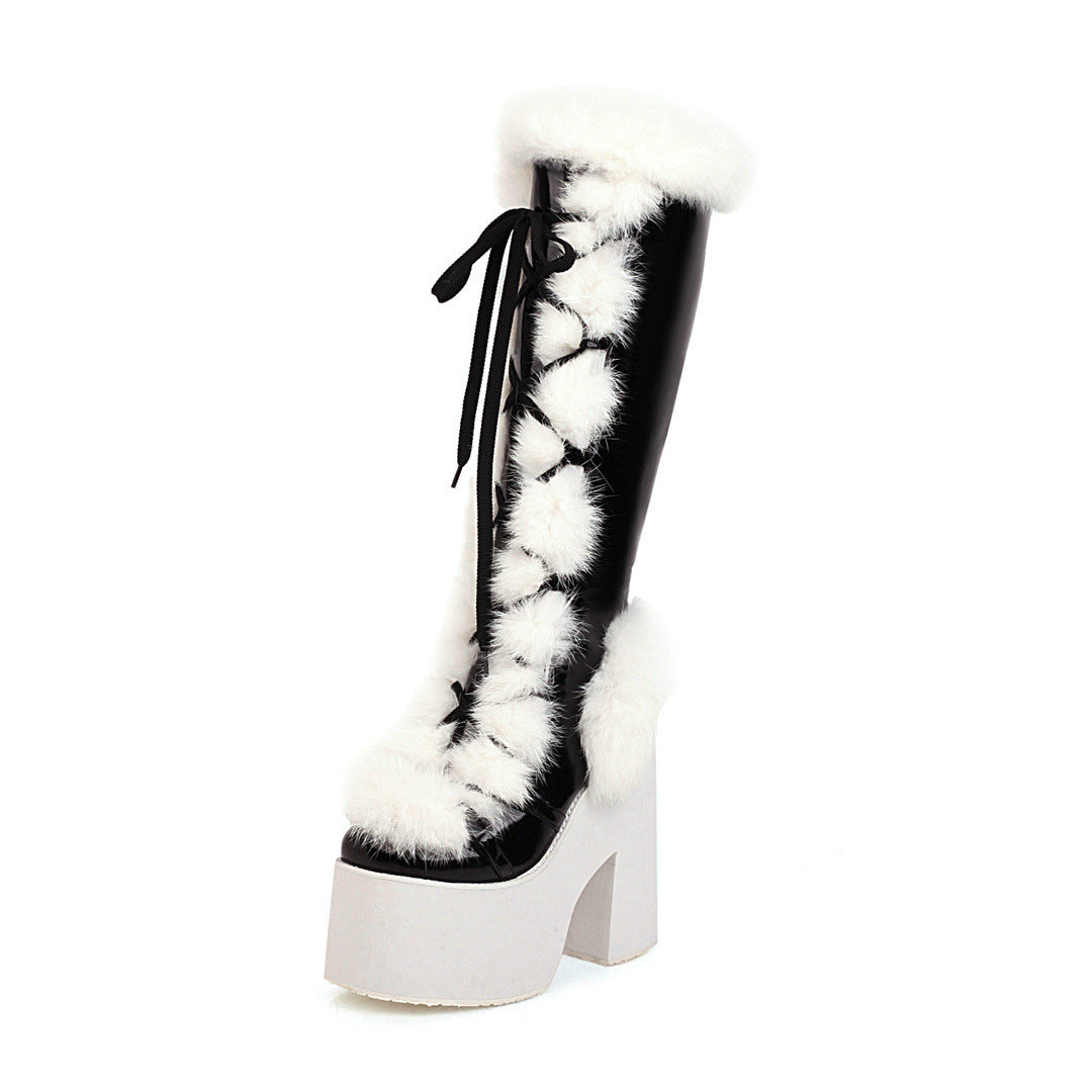 Black and white platform boot with faux fur trim and pom-poms, featuring high chunky heel and lace-up design. Fashionable winter footwear.