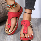 Red women's sandals with decorative stitching, worn with beaded anklets and distressed jeans, showcasing summer fashion footwear trends.