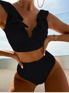 Woman wearing a stylish black ruffled bikini with high-waisted bottoms, accessorized with large hoop earrings and a bracelet, against a sunny backdrop.