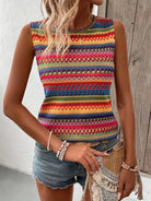 Woman wearing a colorful tribal print sleeveless top with denim shorts, accessorized with beaded bracelets and a woven clutch bag.