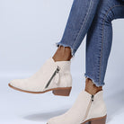 Woman wearing beige suede ankle boots with side zippers, paired with frayed hem blue jeans. Fashionable footwear for casual outfits.