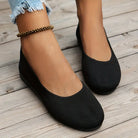 Black knit ballet flats on wooden floor, worn with frayed hem jeans and beaded anklet. Comfortable women's casual footwear, stylish and versatile.