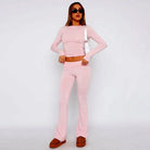 Woman wearing pink two-piece lounge set with long sleeves and flared pants, accessorized with sunglasses and a white shoulder bag. Fashionable casual outfit.