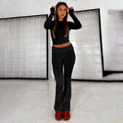 Woman wearing black two-piece lounge set with long sleeves and flared pants, standing indoors. Fashionable casual wear, comfortable home outfit.