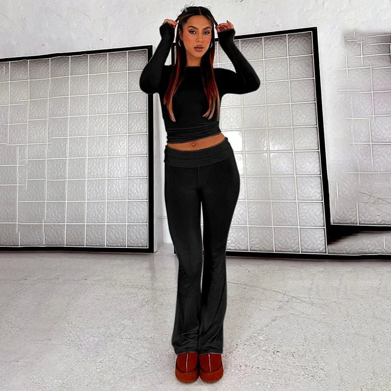 Woman wearing black two-piece lounge set with long sleeves and flared pants, standing indoors. Fashionable casual wear, comfortable home outfit.