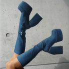 Blue platform knee-high boots with chunky heels against a concrete background, showcasing trendy footwear fashion. Perfect for bold style statements.