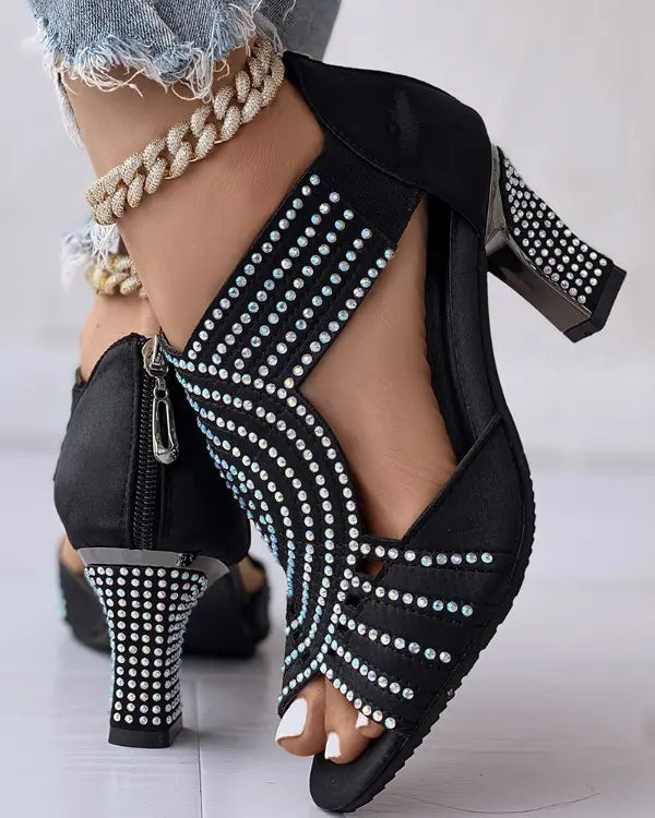 Black high-heeled sandals with rhinestone embellishments, featuring a zipper back and open toe design. Perfect for elegant evening wear and fashion events.