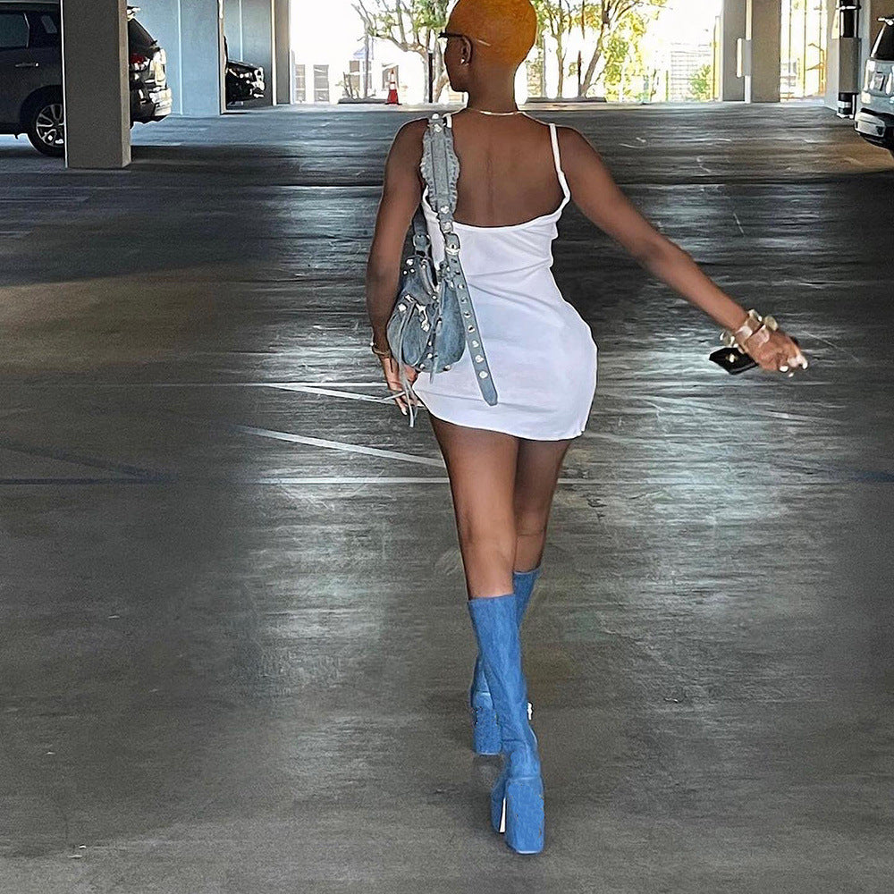 Woman in white mini dress and blue platform boots walking in parking garage, holding a gray handbag. Fashionable urban style, summer outfit.