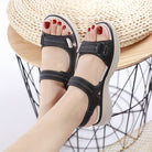 Black women's sandals with adjustable straps, white stitching, and cushioned soles, worn on feet. Perfect for casual summer fashion and comfort.