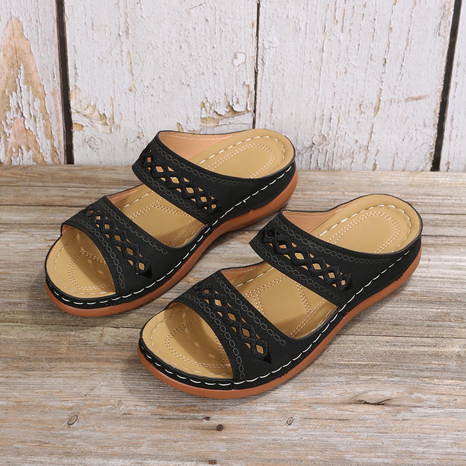 Black leather sandals with cutout design, cushioned tan insoles, and brown soles on rustic wooden background. Comfortable summer footwear.