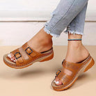 Brown leather sandals with buckle straps on a woman's feet, paired with frayed hem jeans. Comfortable, stylish footwear for casual wear.