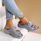 Light blue women's sandals with double buckle straps and cutout design, paired with distressed jeans. Comfortable summer footwear on white steps.