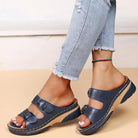 Women's blue leather sandals with double buckle straps, worn with distressed jeans. Comfortable, stylish footwear for casual summer fashion.