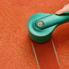 Hand using a green fabric shaver on orange sweater, removing lint and fuzz. Efficient lint remover for clothes, fabric care, sweater maintenance.