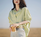 Woman in light green oversized shirt and high-waisted jeans holding a coffee cup outdoors. Fashionable casual outfit, stylish women's clothing.