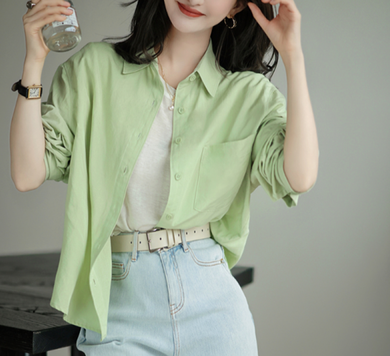 Woman in light green button-up shirt over white top, wearing high-waisted light blue jeans, holding a drink. Fashionable casual outfit.