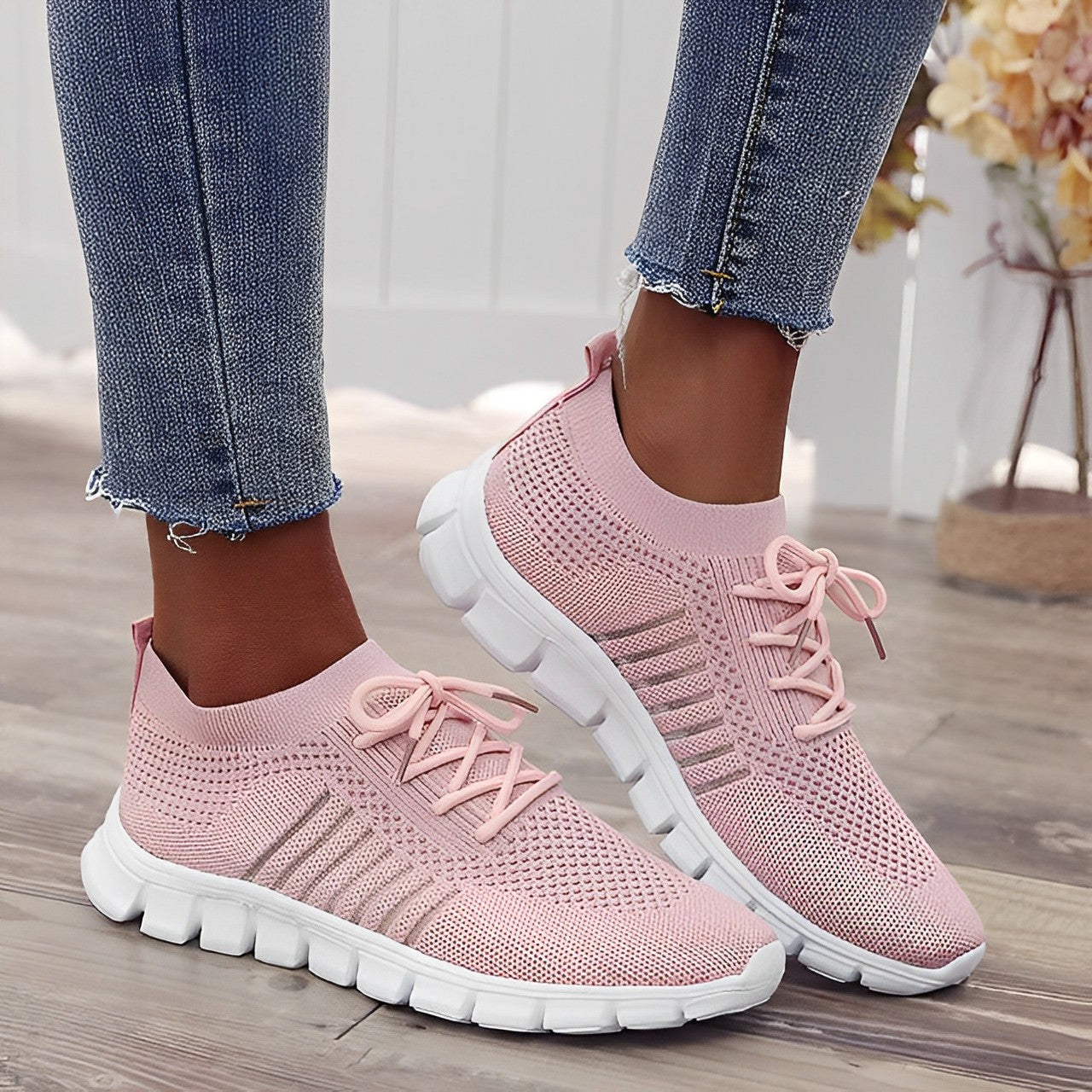 Pink knit slip-on sneakers with white soles, worn with blue jeans. Stylish women's casual footwear, lightweight and breathable design.