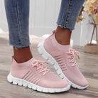 Pink knit slip-on sneakers with white soles, worn with blue jeans. Stylish women's casual footwear, lightweight and breathable design.