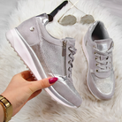 Stylish silver women's sneakers with metallic accents and white soles on a fluffy rug, featuring zipper and lace-up design. Fashionable footwear.