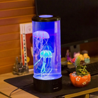 LED jellyfish lamp with glowing blue and pink jellyfish, placed on a desk beside a computer monitor and a cactus plant in a decorative pot.