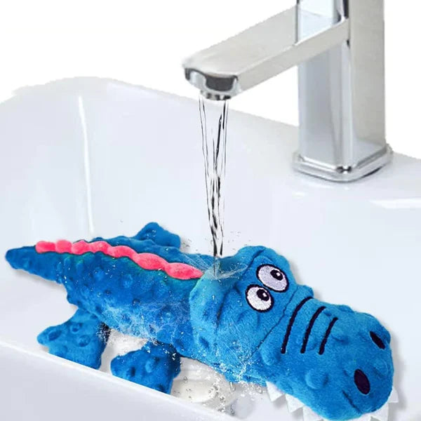 Blue crocodile dog toy being washed under a faucet in a white sink; durable, water-resistant pet toy for cleaning and hygiene.