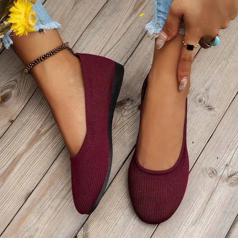 Woman wearing stylish burgundy knit flats with black soles on wooden floor, showcasing casual fashion footwear. Perfect for comfortable everyday wear.