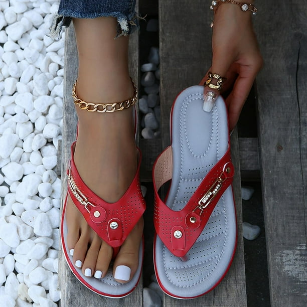 Red women's flip-flops with gold chain detail, worn on a wooden surface with white pebbles. Stylish summer footwear, perfect for casual outings.