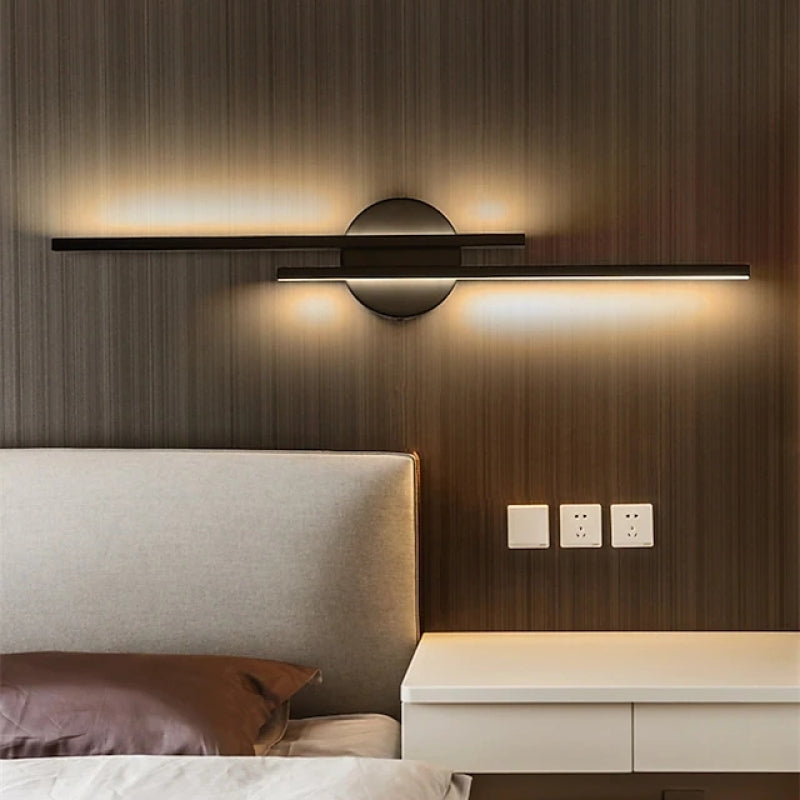 Modern wall sconce with sleek black design and warm LED lighting, mounted above a minimalist nightstand in a contemporary bedroom setting.