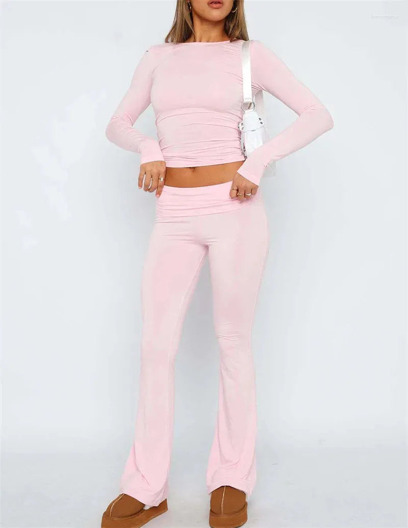 Woman in a stylish pink two-piece outfit with long sleeves and flared pants, accessorized with a white shoulder bag and brown platform shoes.