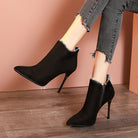 Black suede stiletto ankle boots with side zipper, worn with frayed hem jeans on wooden floor. Fashionable women's footwear, elegant high heels.