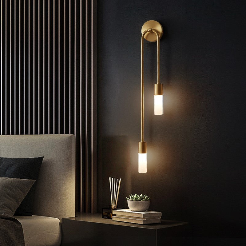 Modern gold wall sconce with dual frosted glass lights, illuminating a stylish bedroom with dark walls and minimalist decor. Elegant lighting fixture.