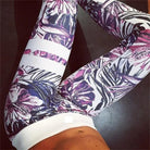 Floral patterned leggings on a person, featuring vibrant purple and pink tropical designs, perfect for yoga or gym workouts. Fashionable activewear.