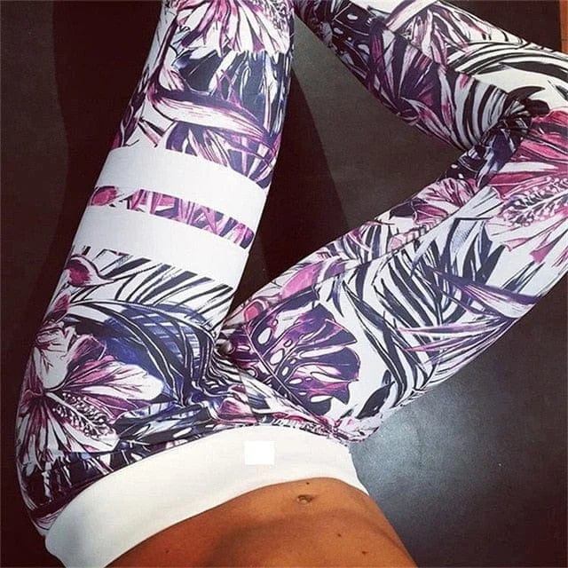 Floral patterned leggings on a person, featuring vibrant purple and pink tropical designs, perfect for yoga or gym workouts. Fashionable activewear.
