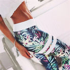 Woman wearing floral patterned athletic leggings and a white crop top, showcasing fitness fashion. Tropical print workout outfit, stylish activewear.