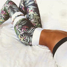 Woman wearing floral patterned green leggings, lying on a white bed. Trendy activewear, stylish workout outfit, floral leggings fashion.
