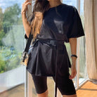 Woman wearing black oversized t-shirt with belt, black cycling shorts, and crossbody bag. Casual summer outfit, trendy fashion style.
