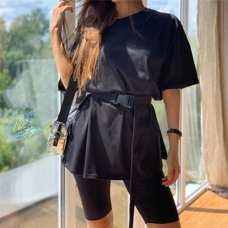 Woman wearing black oversized t-shirt with belt, black cycling shorts, and crossbody bag. Casual summer outfit, trendy fashion style.