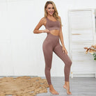 Woman in brown classic-cut sports set, featuring a sleeveless crop top and high-waisted leggings, standing in a modern, minimalist room.