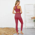 Woman in coral athletic set, featuring a racerback sports bra and high-waisted leggings, standing in a modern room. Fitness fashion, activewear.