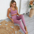 Woman in pink sportswear set, sitting on a wooden floor with floral decor. Fitness outfit, activewear, yoga leggings, and sports bra.