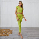 Woman in green open-back sports set, featuring a crop top and high-waisted leggings, standing on a wooden floor with a decorative rug.