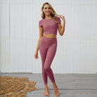 Woman in pink athletic set with open back, standing on wooden floor. Stylish workout outfit, perfect for yoga or gym. Comfortable and trendy activewear.