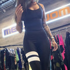 Woman in black athletic jumpsuit with white stripes, shopping in a sportswear store. Trendy fitness apparel, activewear fashion display.