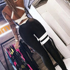 Woman wearing a stylish white and black striped one-piece sports jumpsuit in a modern gym setting, showcasing fitness fashion trends.