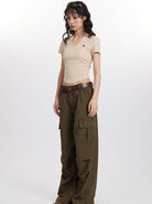 Woman wearing beige V-neck t-shirt and olive cargo pants with brown belt, standing against white background. Fashionable casual outfit, trendy style.