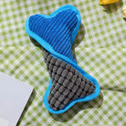 Blue and gray dog bone toy with textured fabric on a green checkered background. Durable pet chew toy for dogs, perfect for play and training.