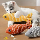 Cute kitten playing with colorful fish-shaped cat toys on wooden floor. Interactive pet toys, zigzag pattern, playful cat accessories.