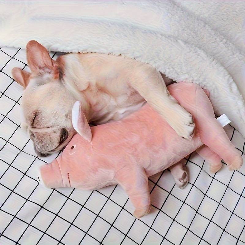 French Bulldog puppy sleeping with pink pig plush toy under a cozy blanket on a checkered bed. Cute dog, pet comfort, adorable animal companionship.