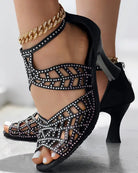 Black strappy high heel sandals with rhinestone embellishments, featuring a gold anklet. Perfect for elegant evening wear and fashion-forward style.