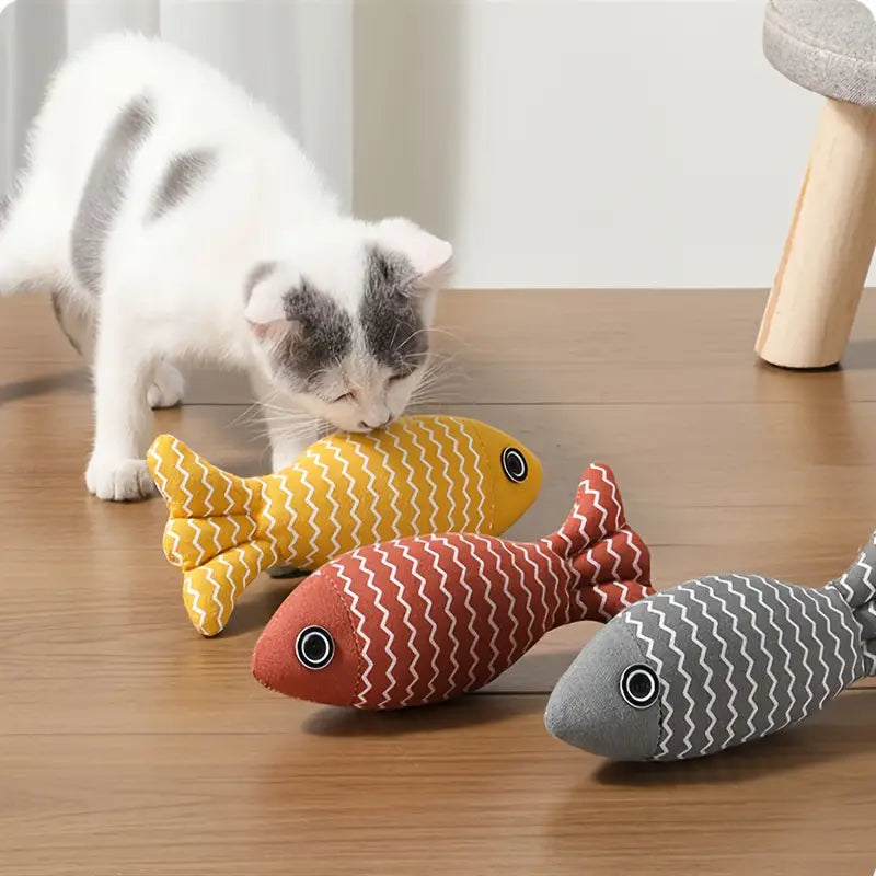 Kitten playing with colorful fish-shaped cat toys on wooden floor; interactive pet toys for cats; yellow, red, and gray plush fish.